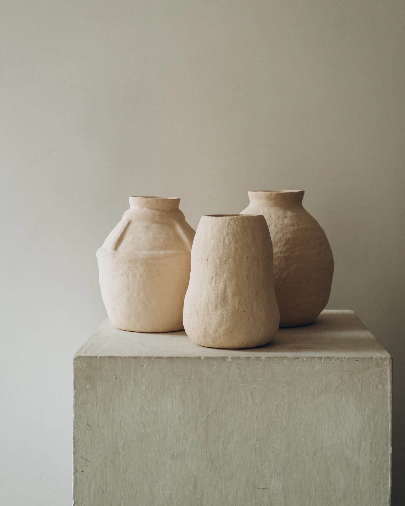 Trio de vasos de cerâmica artesanal em tons de areia sobre pedestal
